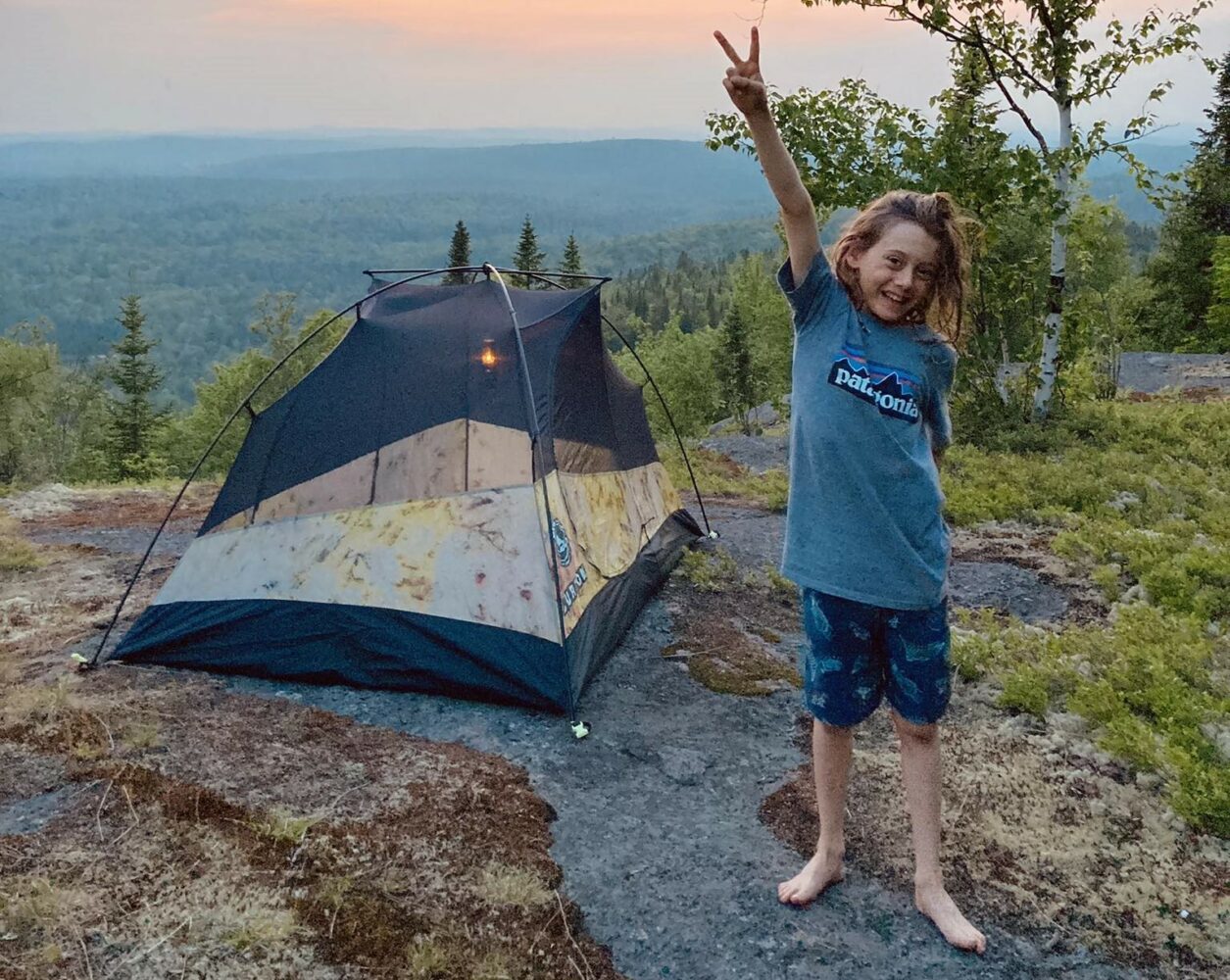 un jeune garçon pose devant une tente au coucher de soleil