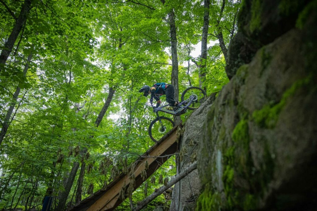 Un homme en vélo de montagne dévale une structure de bois en forêt