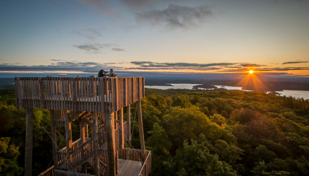 Deux randonneurs admirent le coucher de soleil du haut du plateforme en bois.