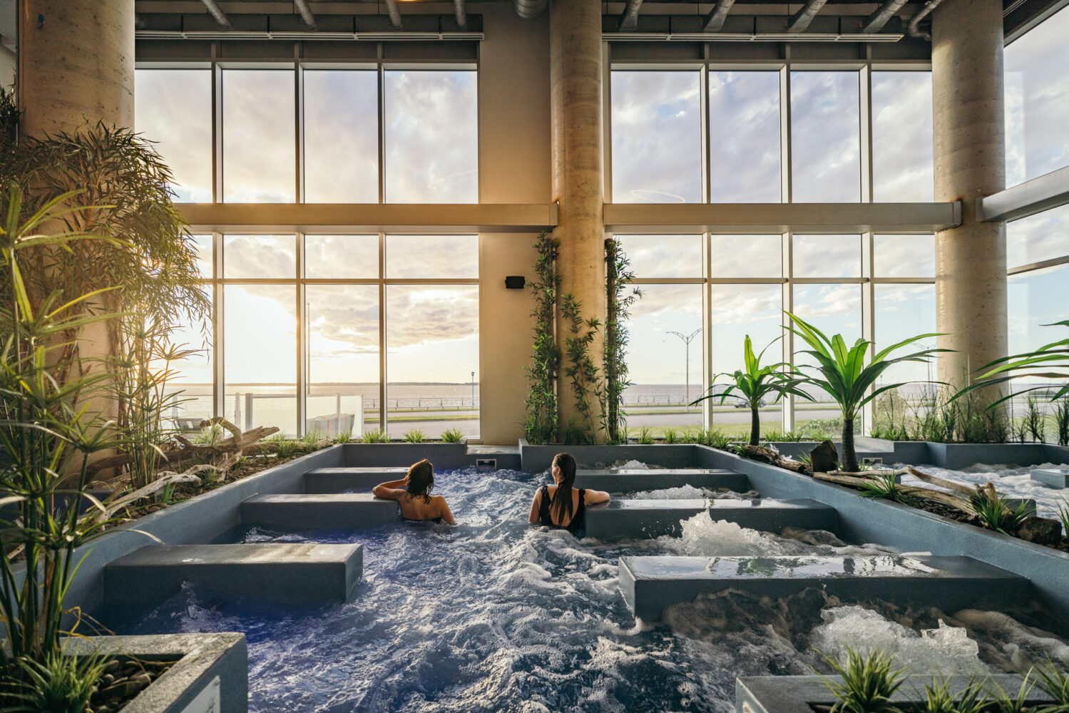 Des gens sont dans une piscine et regardent par les grandes baies vitrées l'extérieur.