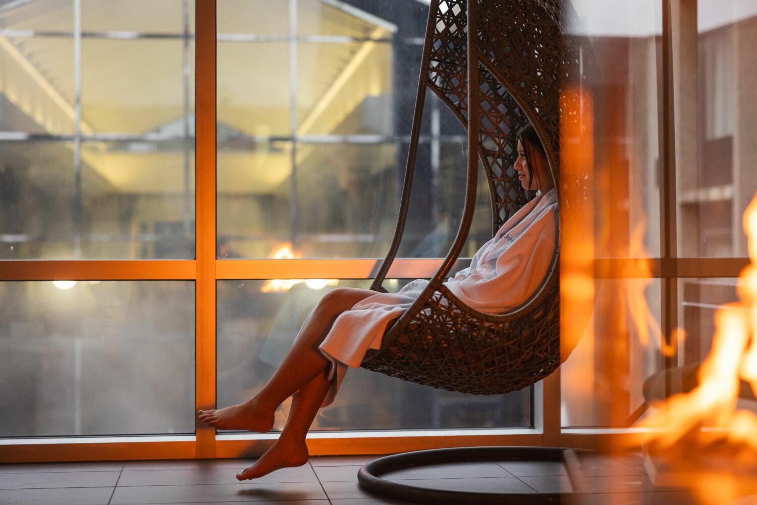 Une dame assise dans une chaise ronde dans un spa, sur le bord d'un feu.