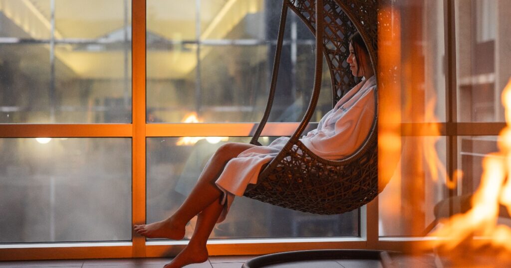 Une femme en peignoir dans une chaise suspendue, relaxant dans les installations intérieures d'Universpa Nordik.