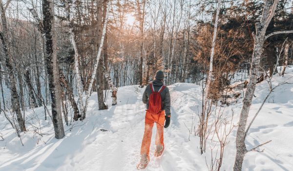 Snowshoeing people in winter forest with snow covered trees on snowy day. Man on hike in snow hiking in snowshoes living healthy active outdoor lifestyle